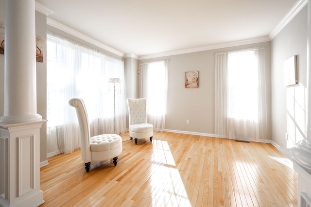 sitting room featuring decorative columns, baseboards, crown molding, and hardwood / wood-style flooring