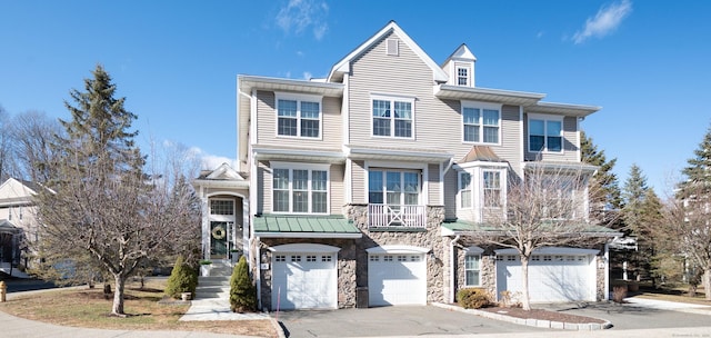 townhome / multi-family property featuring a garage, stone siding, driveway, and a standing seam roof