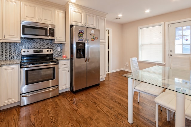 kitchen with stainless steel appliances, dark wood-type flooring, backsplash, and light stone countertops