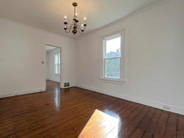 empty room with dark hardwood / wood-style floors, crown molding, and a chandelier