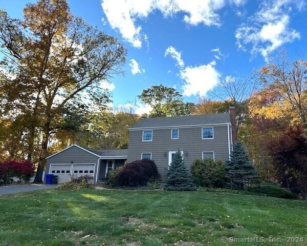 view of front of house featuring aphalt driveway, an attached garage, a chimney, and a front yard