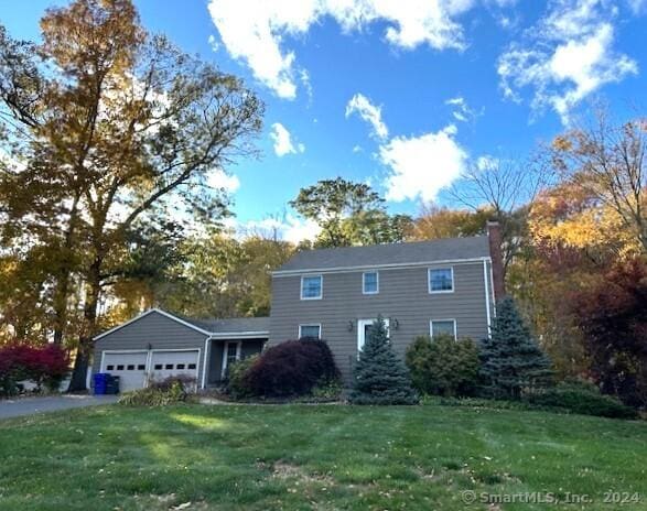 view of front of home featuring a front lawn, an attached garage, a chimney, and aphalt driveway