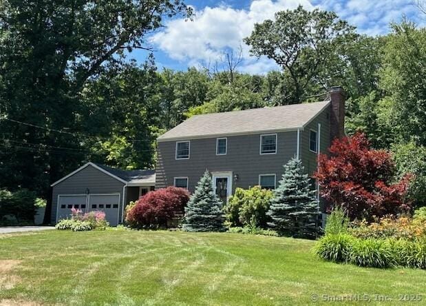 colonial-style house featuring a garage, a chimney, and a front lawn