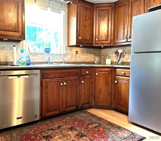 kitchen with brown cabinetry, light wood-style flooring, a sink, appliances with stainless steel finishes, and backsplash