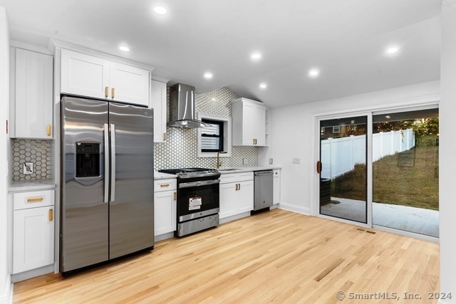 kitchen with white cabinetry, appliances with stainless steel finishes, tasteful backsplash, light hardwood / wood-style flooring, and wall chimney range hood