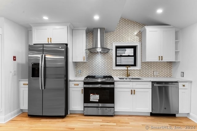 kitchen with light hardwood / wood-style floors, wall chimney exhaust hood, sink, white cabinetry, and appliances with stainless steel finishes