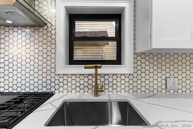 kitchen with tasteful backsplash, white cabinetry, light stone countertops, sink, and wall chimney exhaust hood