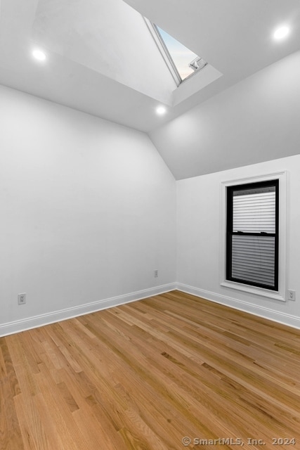 additional living space featuring lofted ceiling with skylight and hardwood / wood-style floors