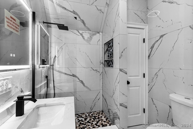 bathroom with tile walls, tiled shower, toilet, and vanity