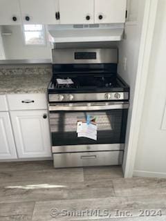 kitchen featuring stainless steel gas range oven, white cabinetry, ventilation hood, and light stone counters