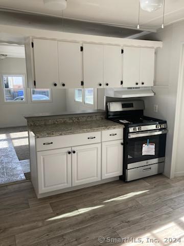 kitchen featuring white cabinets, stainless steel range with gas stovetop, dark wood-type flooring, and range hood