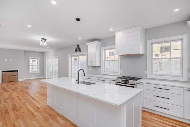 kitchen with stainless steel gas range oven, a kitchen island with sink, sink, and decorative light fixtures