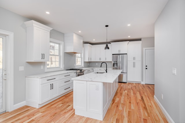 kitchen with a kitchen island with sink, hanging light fixtures, sink, light wood-type flooring, and stainless steel appliances