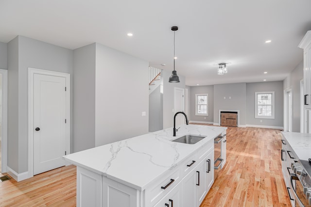 kitchen with a center island with sink, sink, light stone countertops, decorative light fixtures, and light hardwood / wood-style floors