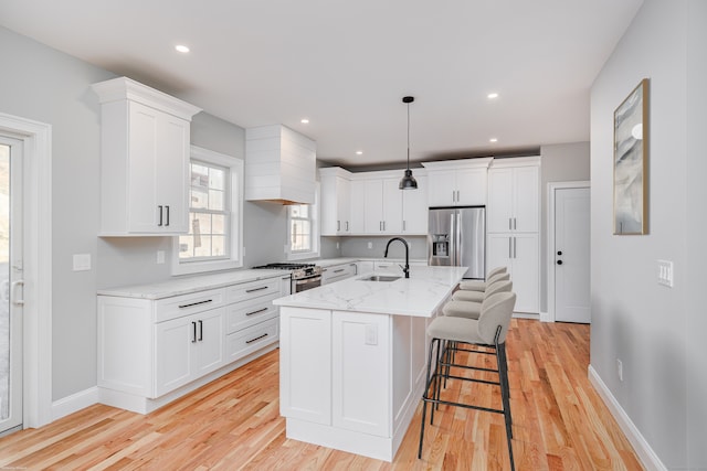 kitchen with a center island with sink, sink, light hardwood / wood-style floors, white cabinetry, and stainless steel appliances