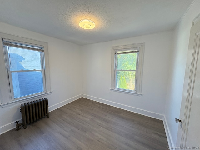 empty room with a textured ceiling, dark hardwood / wood-style floors, and radiator