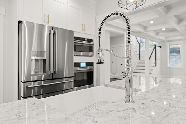 kitchen featuring white cabinets, coffered ceiling, beam ceiling, light stone countertops, and appliances with stainless steel finishes