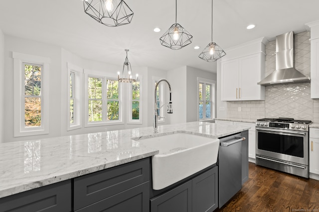 kitchen with stainless steel appliances, white cabinets, wall chimney exhaust hood, hanging light fixtures, and a wealth of natural light