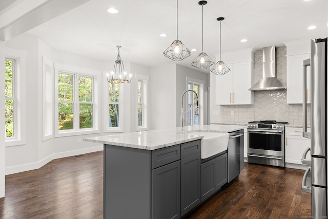 kitchen featuring stainless steel appliances, white cabinetry, sink, wall chimney exhaust hood, and hanging light fixtures