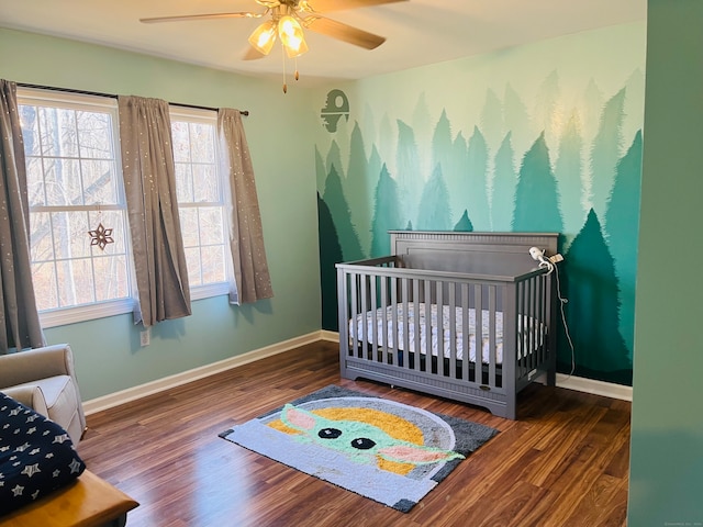 bedroom with ceiling fan, a crib, and dark wood-type flooring