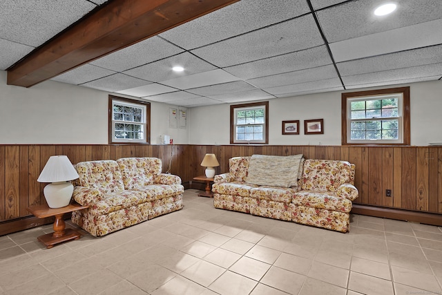 tiled living room with wood walls, a paneled ceiling, and baseboard heating