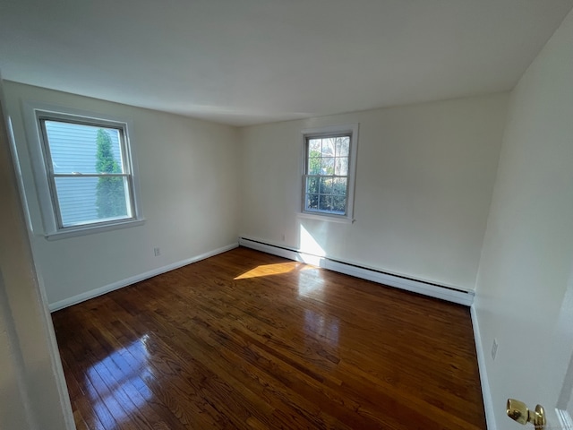 unfurnished room featuring a healthy amount of sunlight, dark wood-type flooring, and a baseboard heating unit