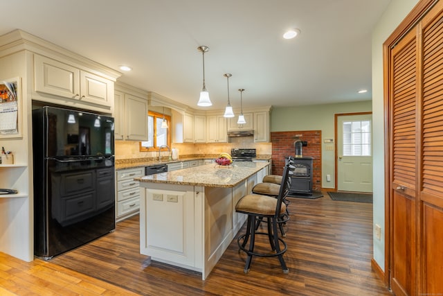 kitchen featuring black appliances, decorative light fixtures, a center island, and dark hardwood / wood-style flooring