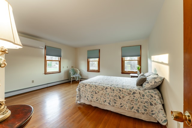 bedroom featuring multiple windows, light hardwood / wood-style flooring, a wall mounted AC, and a baseboard heating unit