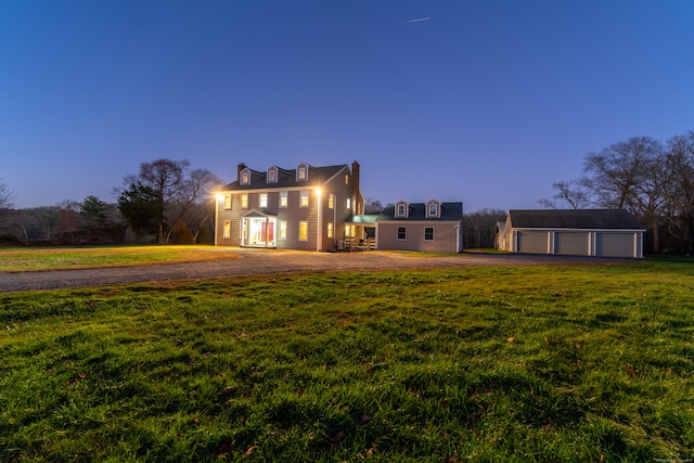 back house at dusk featuring a garage, an outbuilding, and a yard