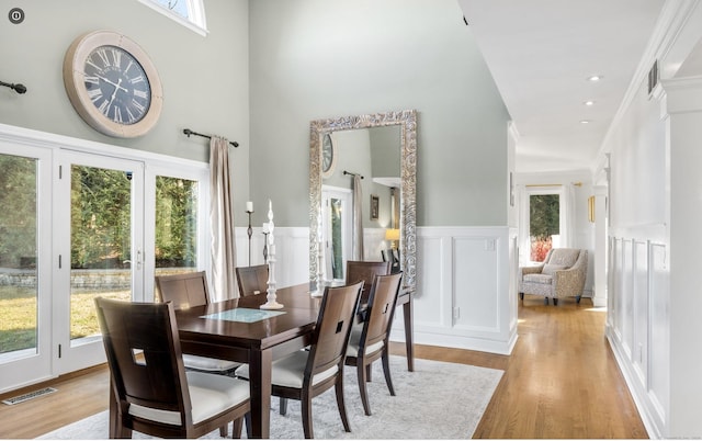 dining space with a high ceiling, a decorative wall, a wainscoted wall, light wood-type flooring, and visible vents