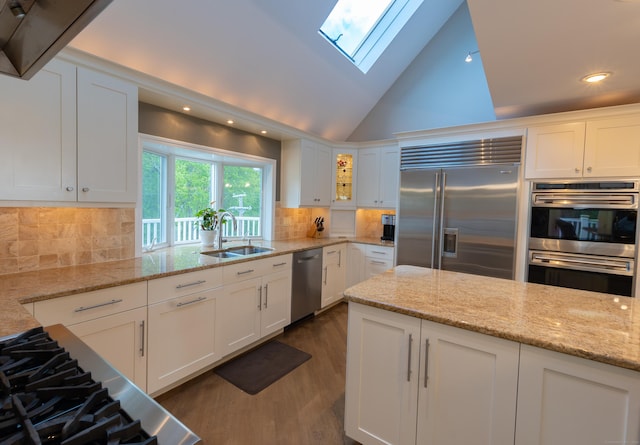 kitchen with white cabinets, appliances with stainless steel finishes, vaulted ceiling with skylight, dark wood finished floors, and recessed lighting