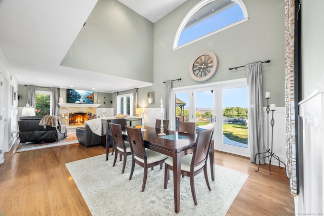 dining space with a towering ceiling, a warm lit fireplace, and light wood-style floors