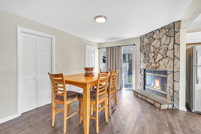 dining space featuring a stone fireplace and dark wood-type flooring