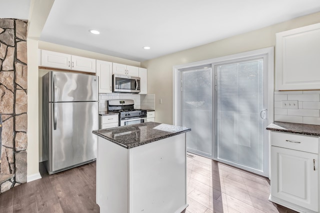 kitchen featuring white cabinets, light hardwood / wood-style flooring, decorative backsplash, dark stone countertops, and appliances with stainless steel finishes