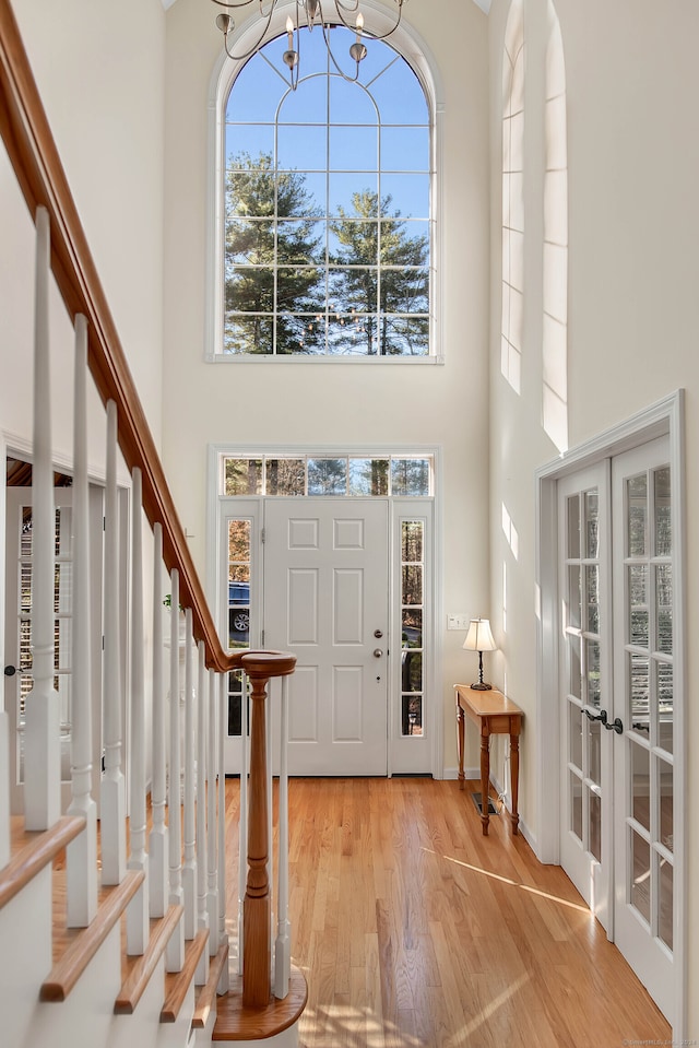 entrance foyer featuring french doors, a towering ceiling, light hardwood / wood-style floors, and an inviting chandelier