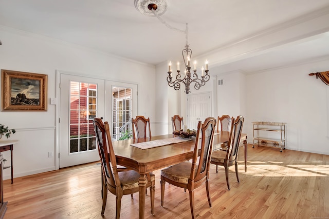 dining room featuring french doors, ornamental molding, a notable chandelier, and light wood-type flooring