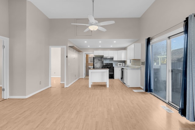 kitchen featuring a towering ceiling, white cabinets, and black appliances