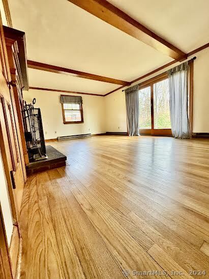 unfurnished living room with light wood-type flooring, beam ceiling, and a baseboard radiator