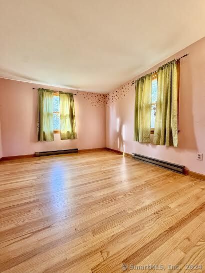 empty room with a healthy amount of sunlight, light hardwood / wood-style flooring, and a baseboard heating unit