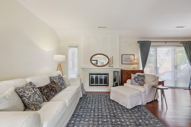 living room featuring lofted ceiling, dark hardwood / wood-style floors, and a brick fireplace