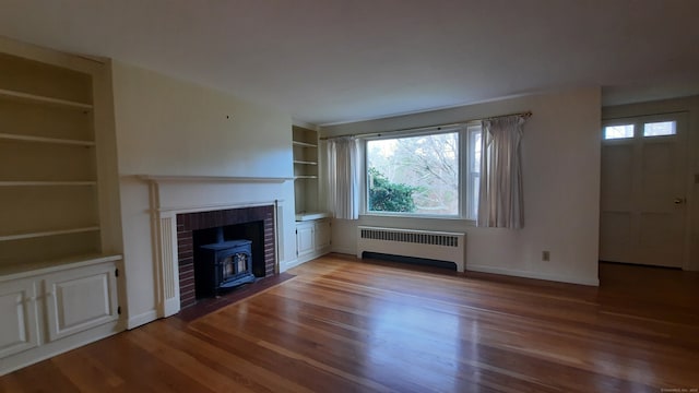 unfurnished living room with radiator heating unit, wood-type flooring, a healthy amount of sunlight, and a wood stove