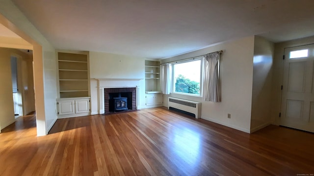 unfurnished living room featuring built in features, radiator, a wood stove, and dark hardwood / wood-style floors