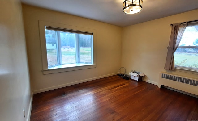 unfurnished room featuring a healthy amount of sunlight, radiator heating unit, and dark hardwood / wood-style flooring