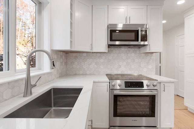 kitchen with white cabinetry, sink, light stone countertops, and stainless steel appliances