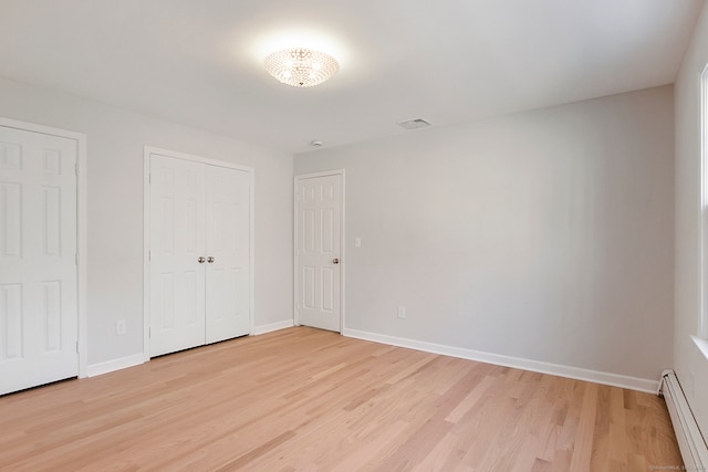 unfurnished bedroom with two closets, a baseboard heating unit, and light hardwood / wood-style floors