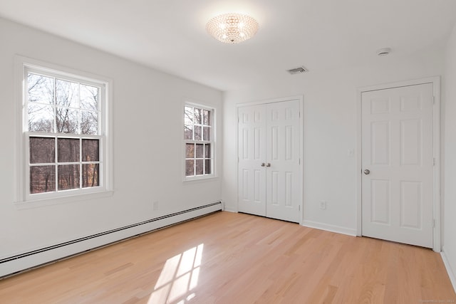 unfurnished bedroom with baseboard heating, light hardwood / wood-style floors, and a notable chandelier