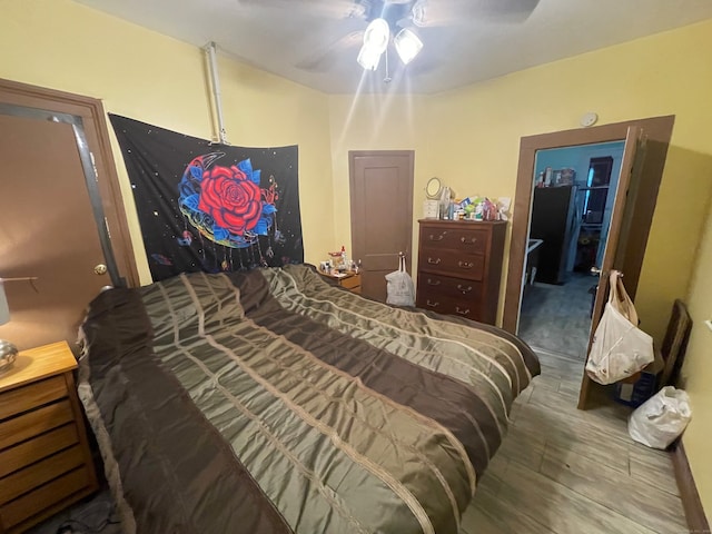 bedroom with wood-type flooring, ceiling fan, and black refrigerator