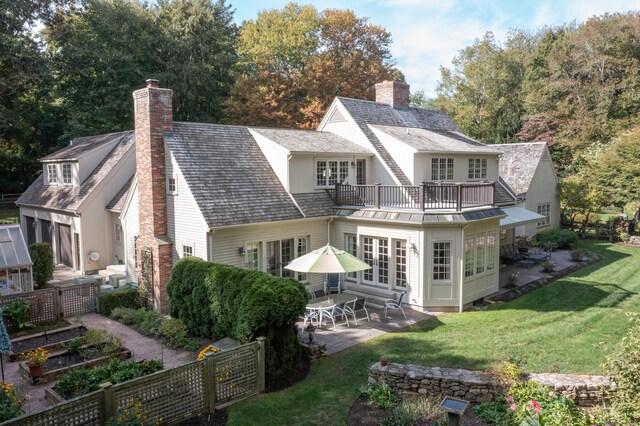 back of house with fence, a chimney, a balcony, a lawn, and a patio