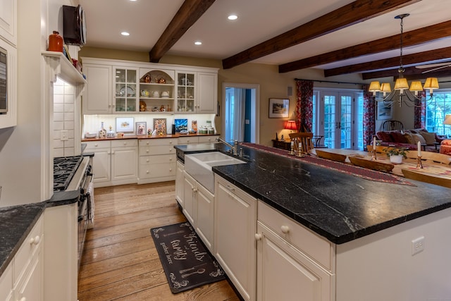 kitchen featuring a kitchen island with sink, beam ceiling, decorative light fixtures, light hardwood / wood-style flooring, and white cabinets