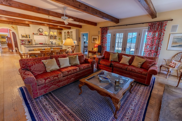 living room with beamed ceiling, light wood-style floors, ceiling fan, french doors, and arched walkways